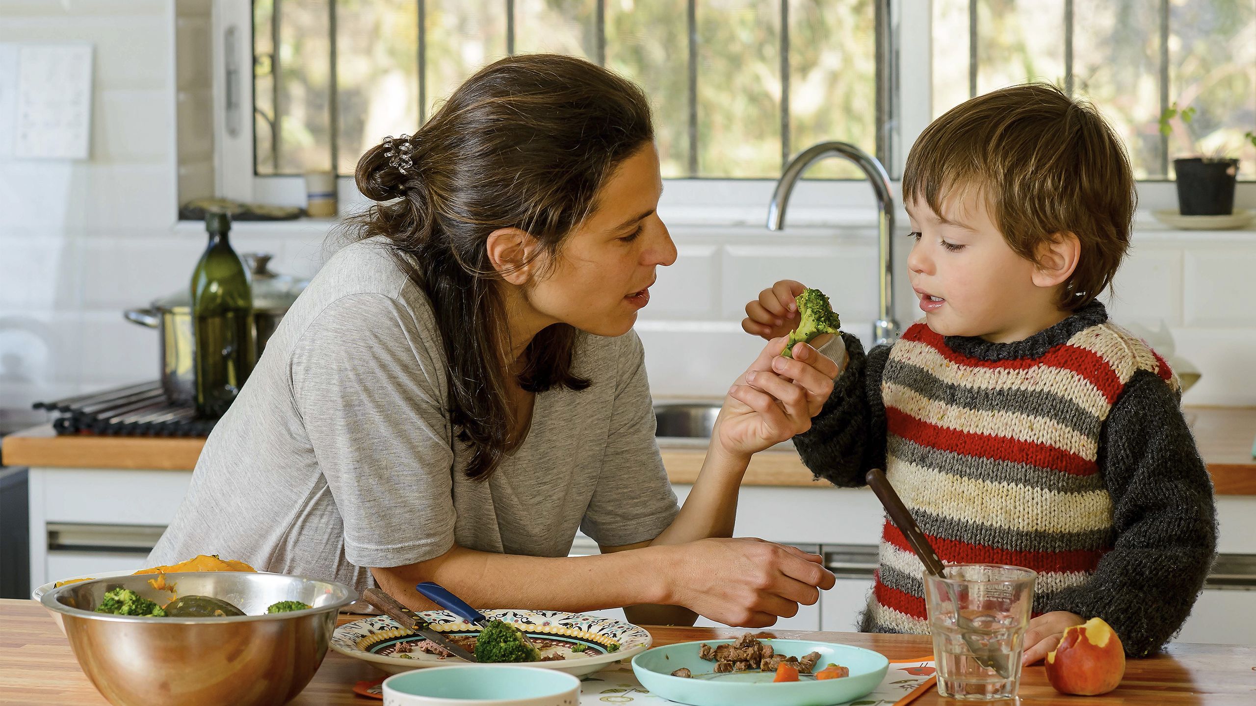 A woman gives broccoli to her son